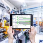 Horizontal_color_image_of_female_hands_holding_a_digital_tablet_in_a_modern_plastic_production_line._Ordering_on-line_from_injection_moulding_factory_on_a_touchscreen_tablet_computer._Large_factory,_industrial_machines,_robots_and_manufacturing_equipment_